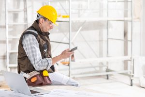 construction worker sitting on desk corner at job site looking at phone