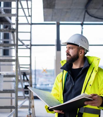 Mature man engineer standing on construction site, holding blueprints.