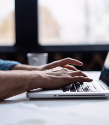 hands typing on laptop at desk in front of windows
