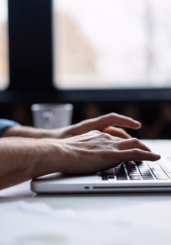 hands typing on laptop at desk in front of windows